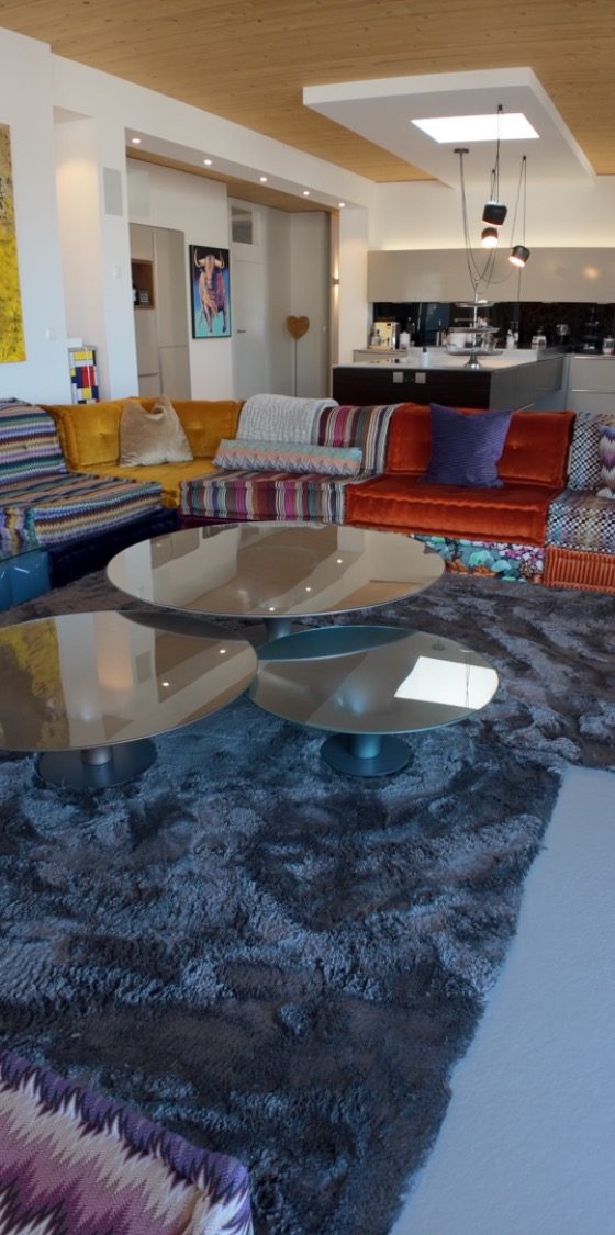 Moderne Wohnung Modern Wohnzimmer mit bunten Sofas, Glastischen und einem Teppich. Kochnische im Hintergrund.