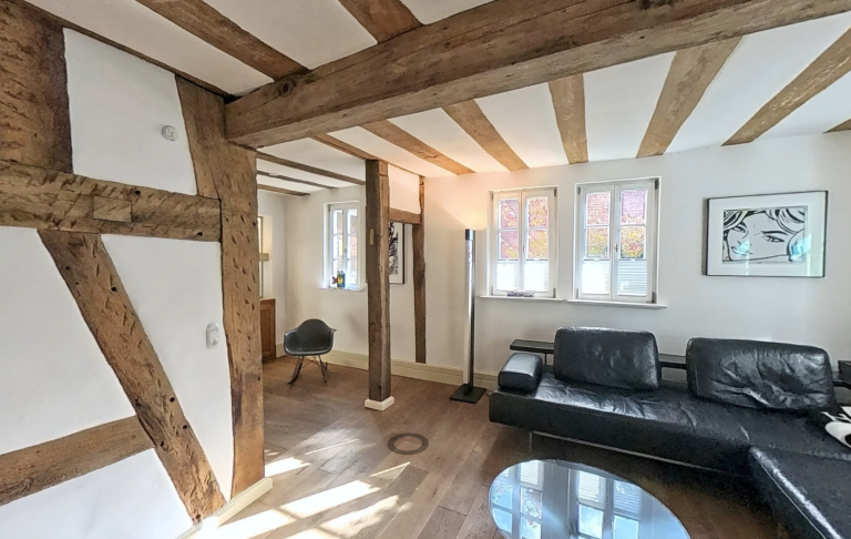 360° Rundgang Moderne Wohnräume mit Holzbalken, schwarzem Sofa und runder Glastisch.